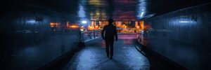 Man walking through dark tunnel towards lighted street.